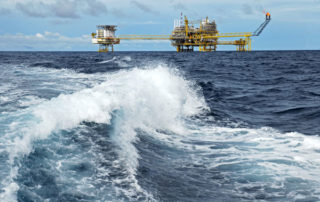 Oil rig out at sea as waves crash in the foreground