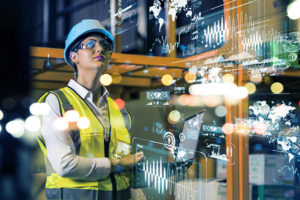 Female engineer in PPE looks at digital displays and lights in workplace