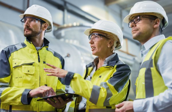 Three Heavy Industry Engineers Stand in Pipe Manufacturing Factory