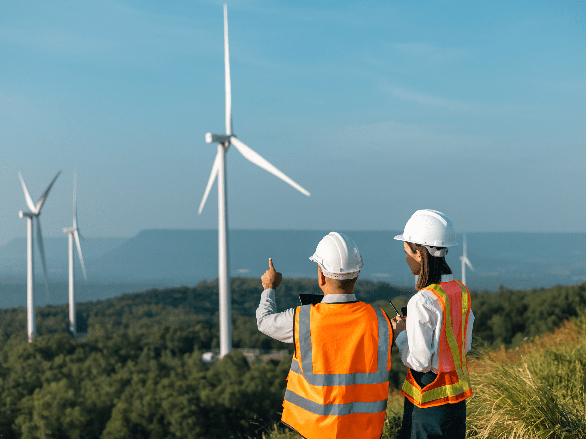 Wind Turbines A Lady And A Man In Orange Vests On A Hill Pointing At Wind Turbines