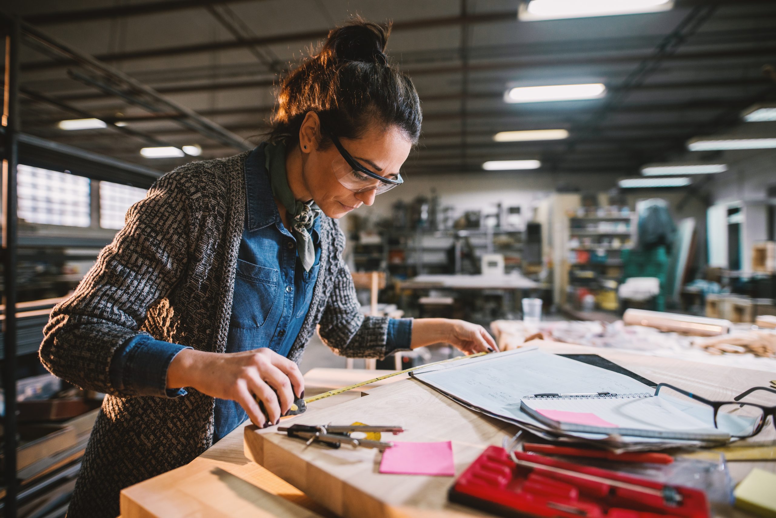 Thoughtful Middle Aged Industrial Female Engineer With Eyeglasses Working With A Tape Measure In The Workshop.