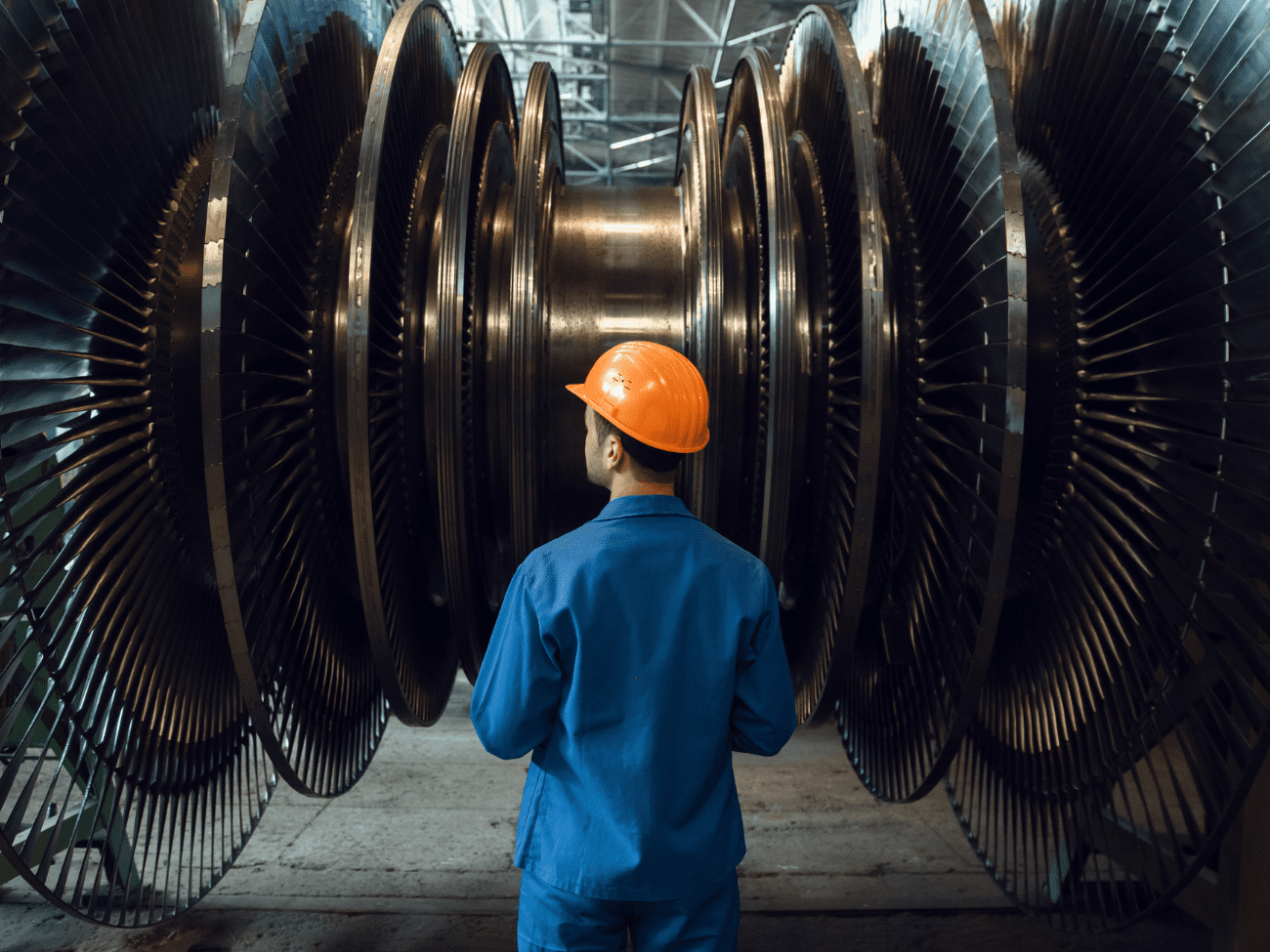 Man In Orange Hard Hat Looking At Large Metal Wheels