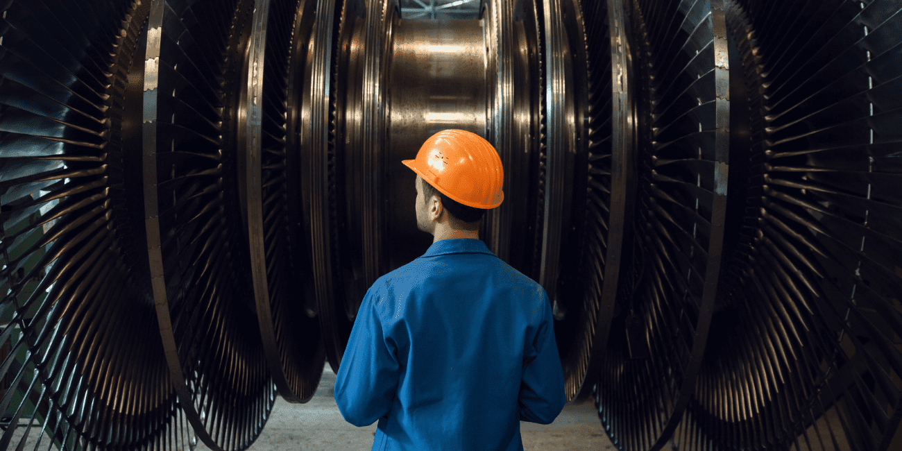 Man In Orange Hard Hat Looking At Large Metal Wheels  Aspect Ratio 1160 580