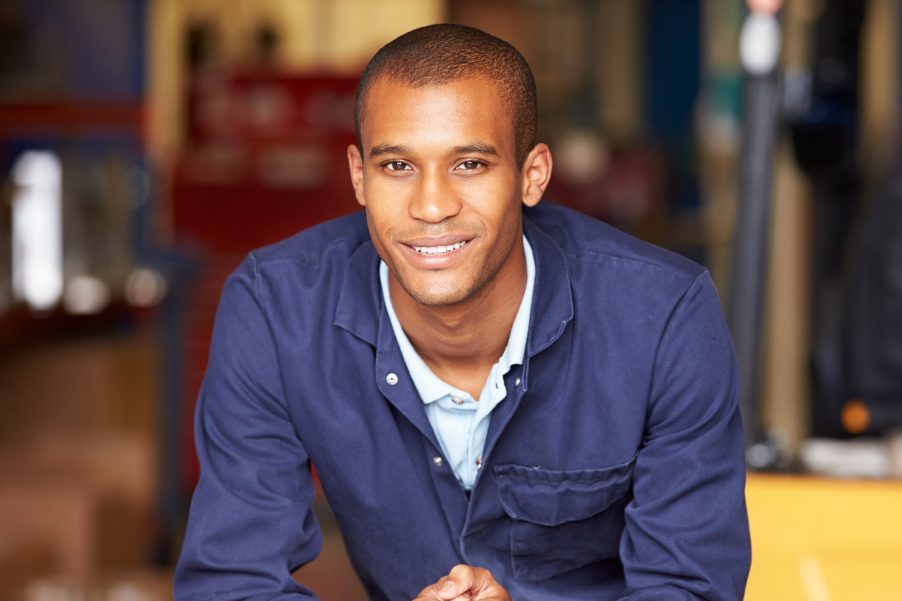 Smiling Man Sitting At A Table In A Warehouse Aspect Ratio 1200 800