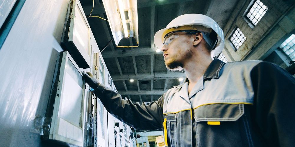 A Person In A Hard Hat Standing In Front Of A Control Panel Aspect Ratio 1160 580