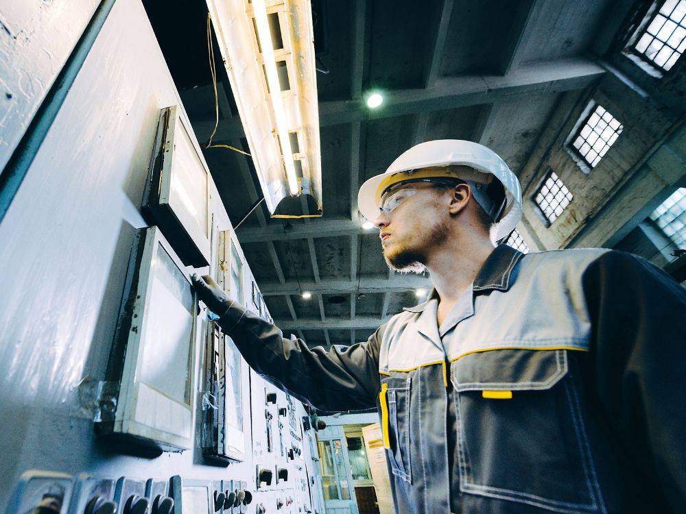A Person In A Hard Hat Standing In Front Of A Control Panel