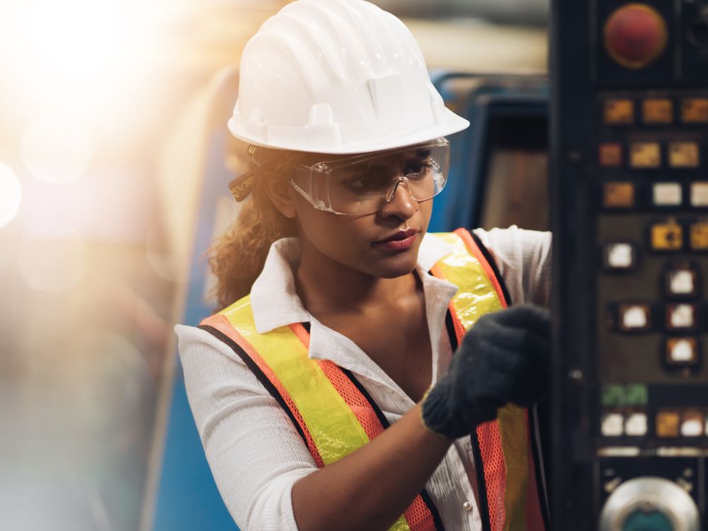 A Woman In A Hard Hat And Safety Glasses Working On A Machine