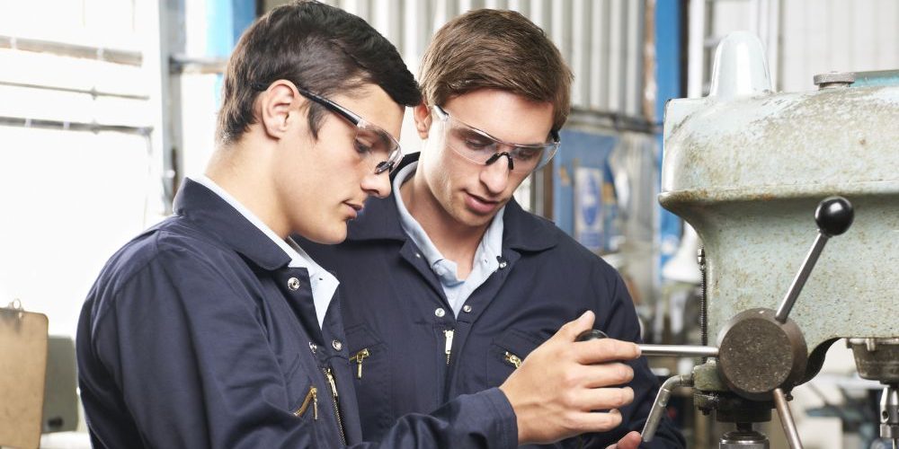 Two Men Working On A Machine In A Factory Aspect Ratio 1160 580