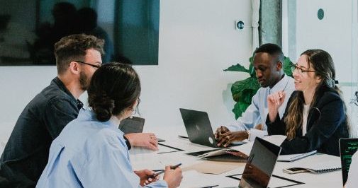 A Group Of People Sitting Around A Table In An Office