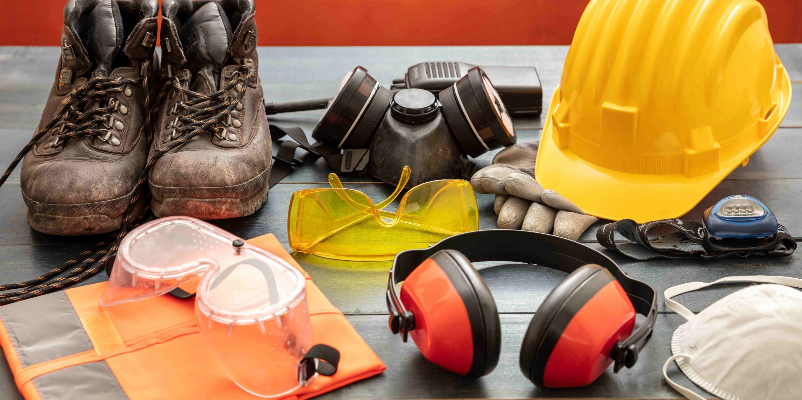 Work Safety PPE Protection Equipment. Industrial Protective Gear On Wooden Table, Red Color Background.