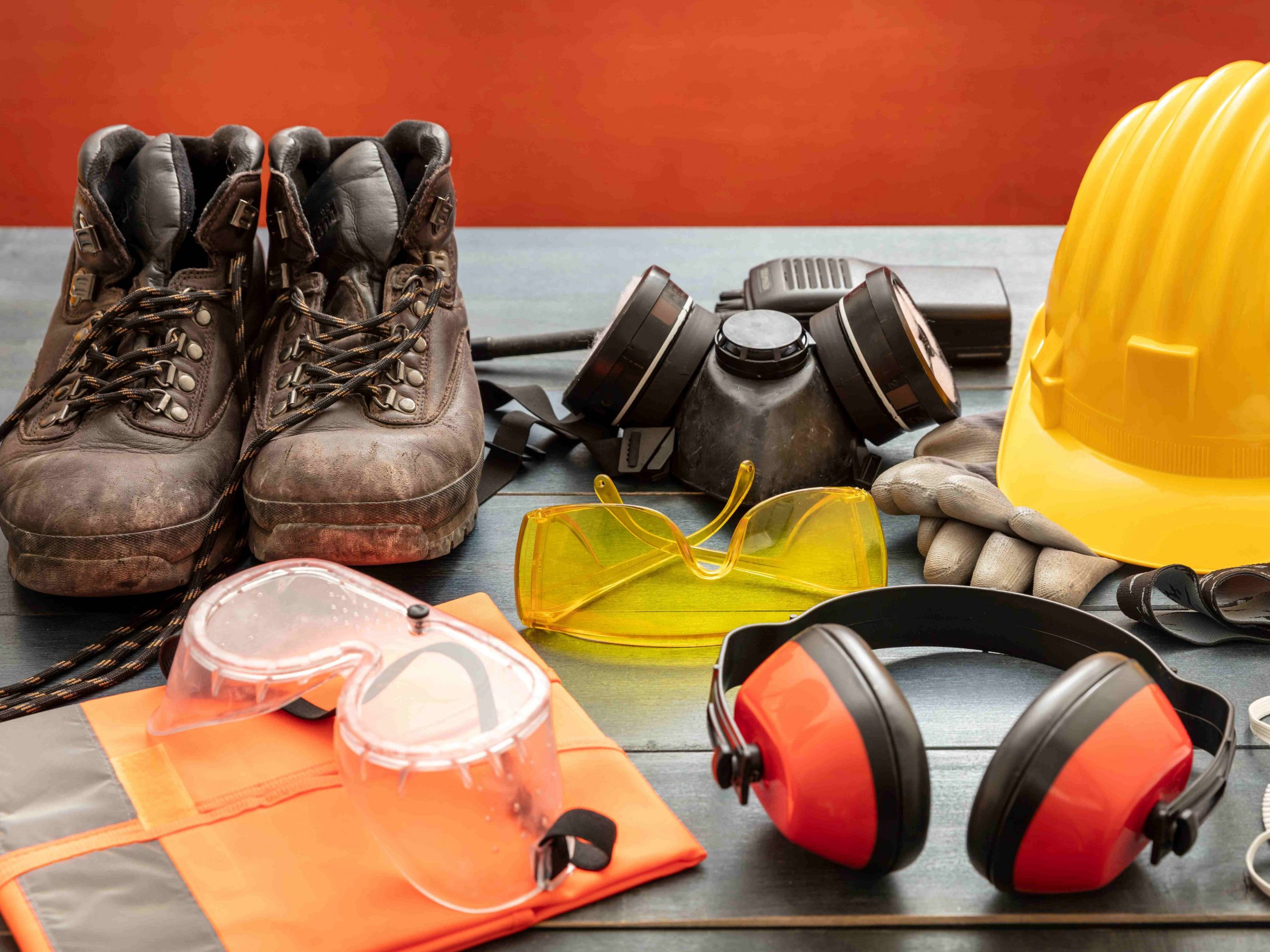 Work Safety PPE Protection Equipment. Industrial Protective Gear On Wooden Table, Red Color Background.