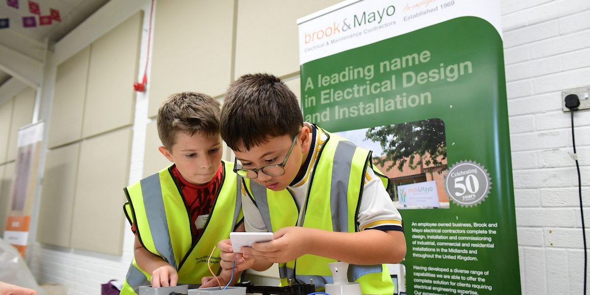 C&EW 2024  Two Young Boys Wearing High Visibility Vests Work Together On An Electrical Project At A Workshop Table.