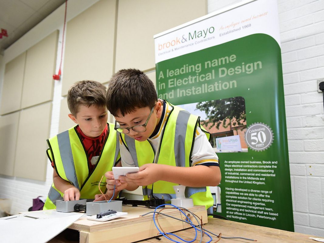 C&EW 2024  Two Young Boys Wearing High Visibility Vests Work Together On An Electrical Project At A Workshop Table.