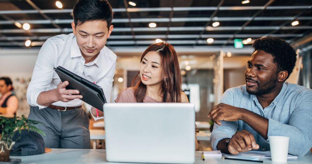 Three People Working On A Laptop In An Office