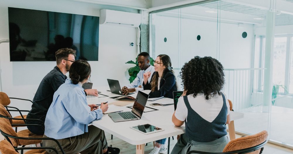 A Group Of People Sitting Around A Table In An Office