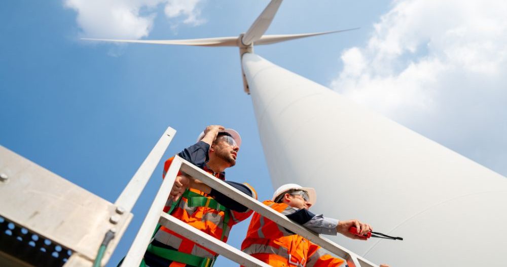 Two People Standing On A Platform Next To A Wind Turbine